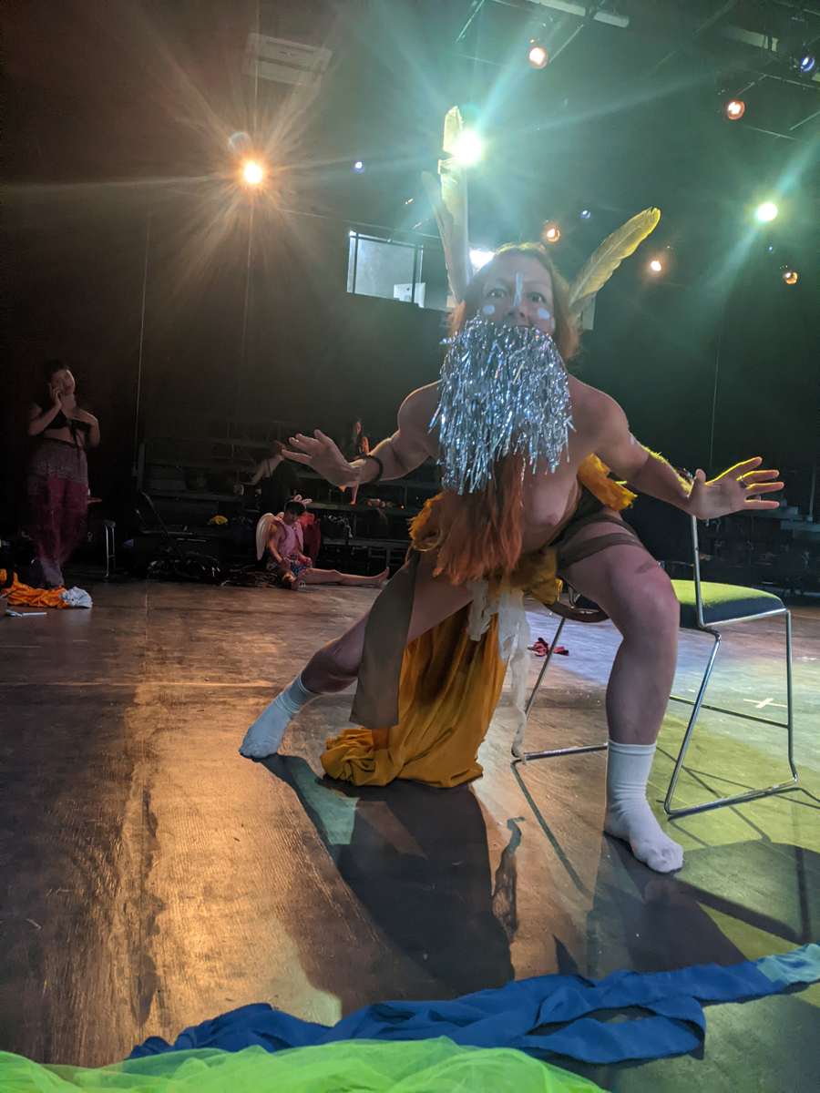 Crouching low with open hands, tinsel beard catching the stage light
