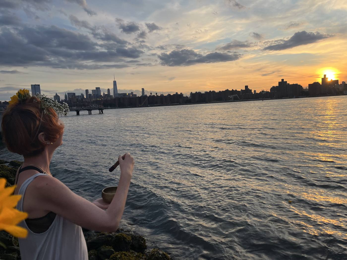Dasha in a flower crown sounding a singing bowl over the East River at sunset, Summer Solstice Ritual