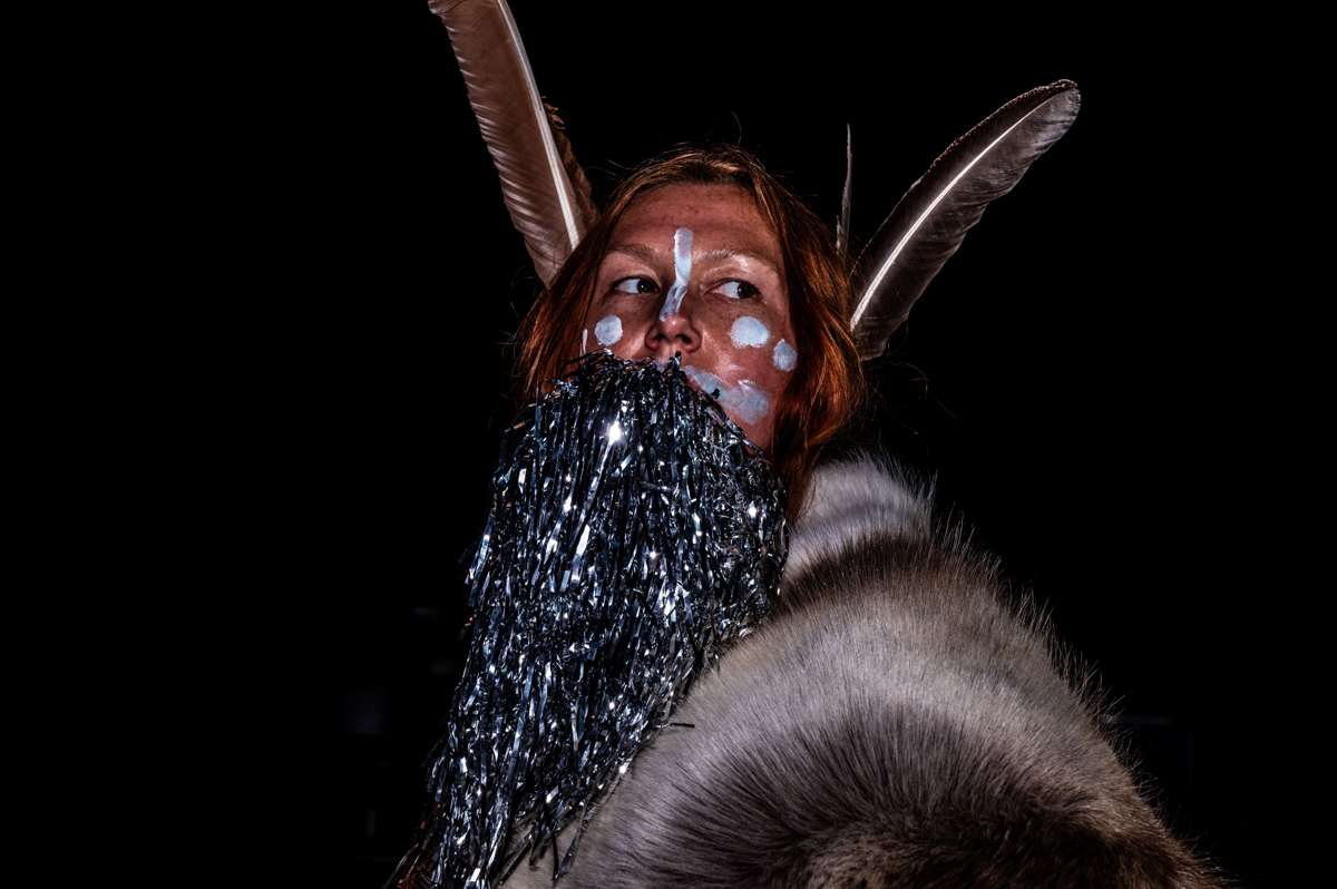 Dasha in feathers, white face paint, and a silver tinsel beard, holding a reindeer skin — La Pocha Nostra workshop, Mérida