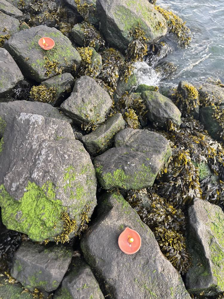 Small clay oil lamps burning on seaweed-covered river rocks