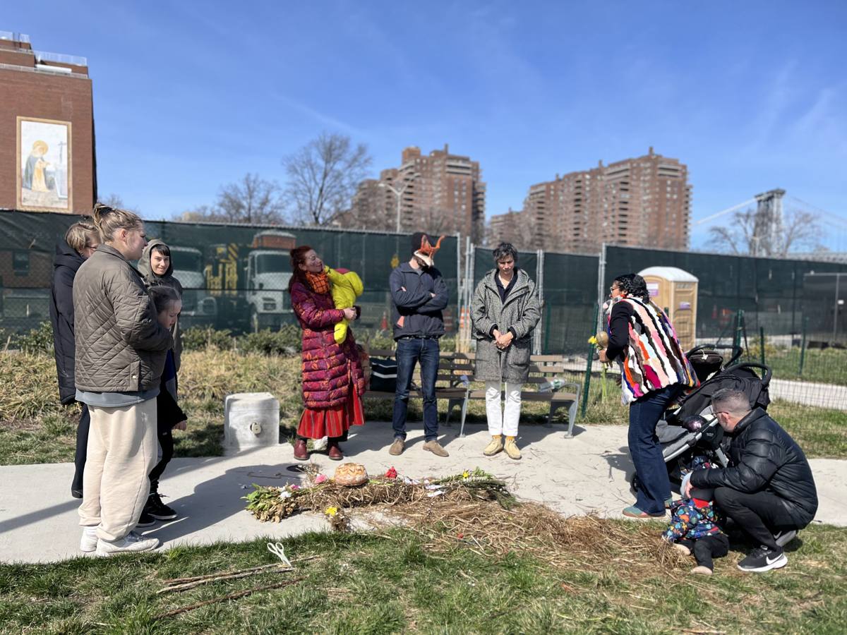 The community gathered in a circle around the effigy laid on the ground with bread and flowers, Dasha holding her child
