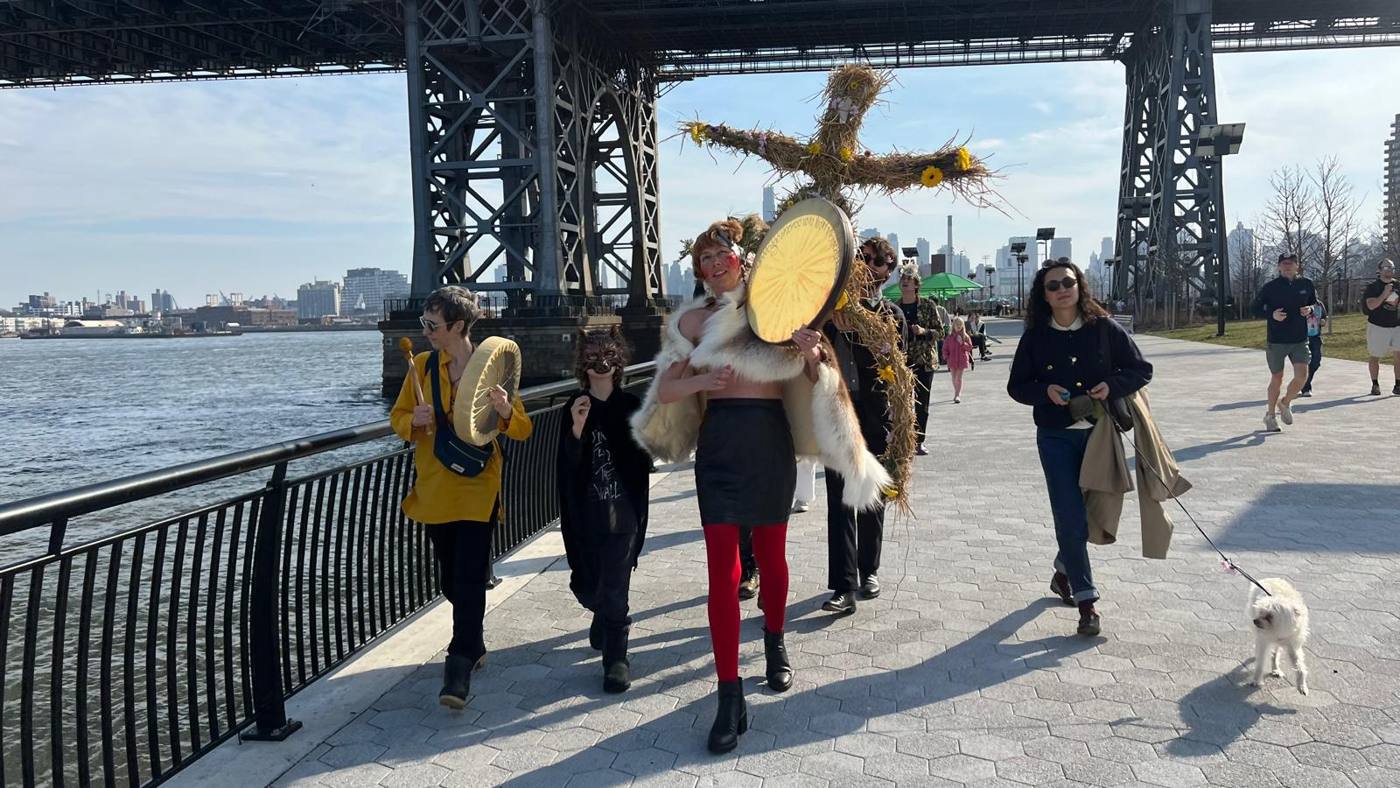 The full procession with drums, masks, and the straw effigy carried along the East River under the Williamsburg Bridge, Ascent Ritual