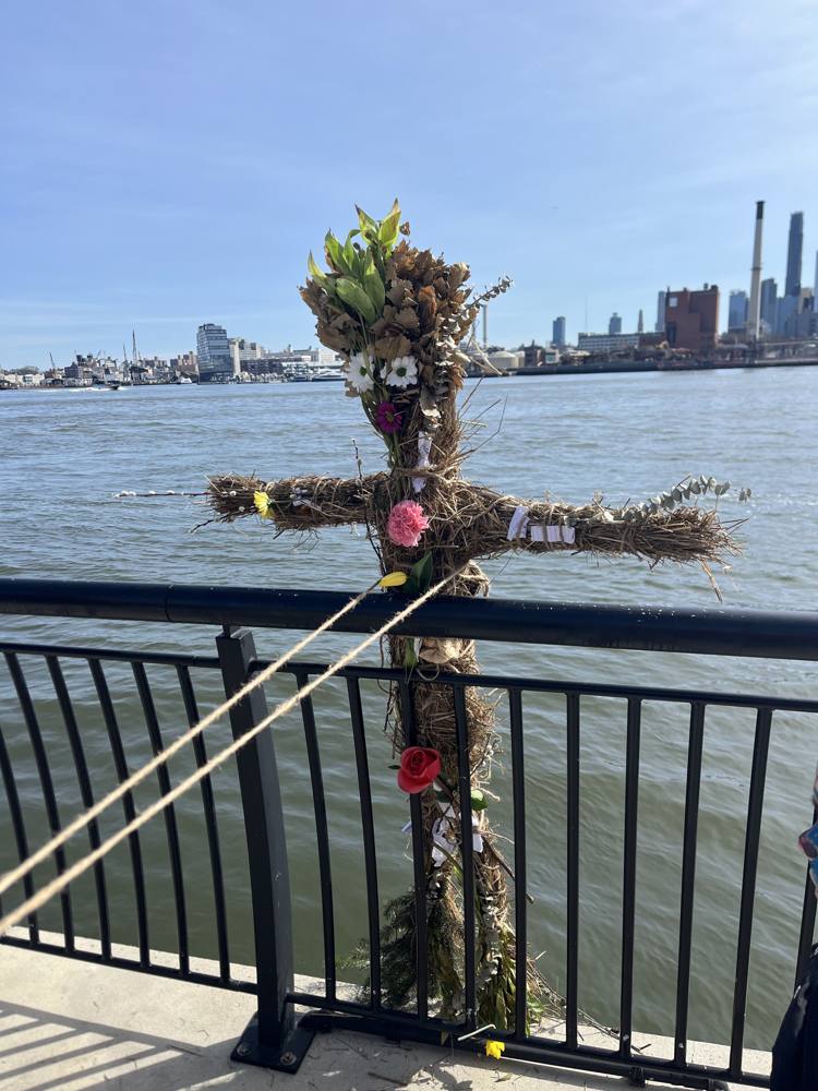 The straw effigy tied upright at the railing above the East River, dressed with flowers and paper wishes, before the burn